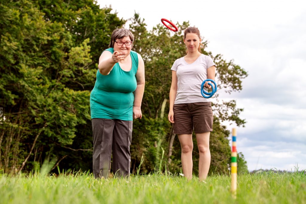 A lady with a disability is playing a ring throwing game with her support worker outdoor.