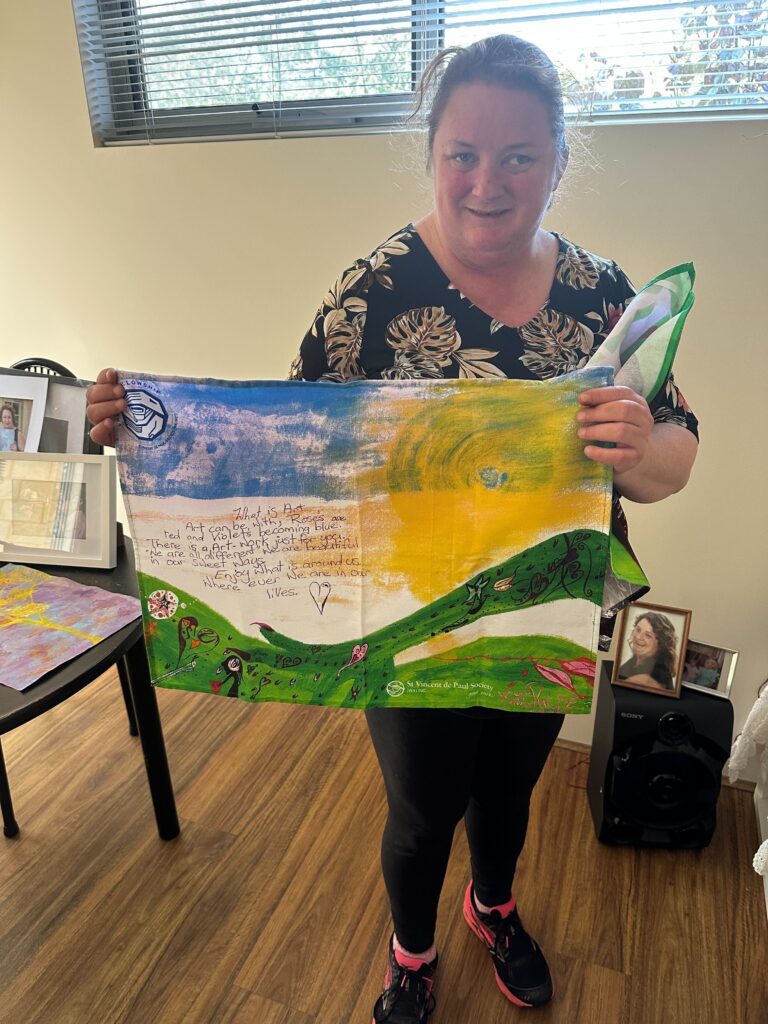 Photograph of Emma (participant) holding her artwork which has been printed on a tea towel.